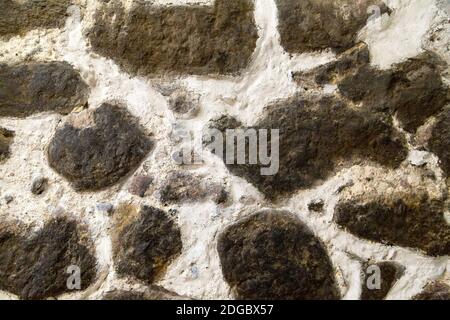 Pareti in pietra testurizzata costruite con grandi pietre grezze tenute insieme da grumi scuri di limesto di cemento bianco Foto Stock