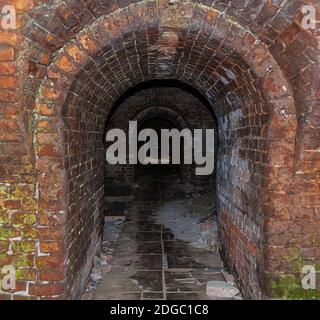 Tunnel di mattoni scuri della catacomba con vista dell'ingresso ad arco al buio del vecchio edificio Foto Stock