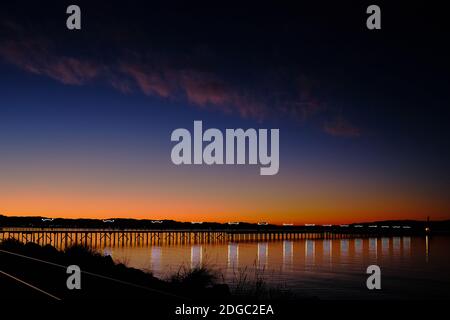 Bella mattina invernale si riparte a White Rock, British Columbia. Le lampade illuminate e scintillanti sul molo di legno si riflettono nelle acque calme della Baia di Semiahmoo Foto Stock