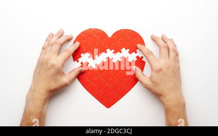 Mani corrispondenti a due pezzi di puzzle a forma di cuore su sfondo bianco, vista dall'alto Foto Stock