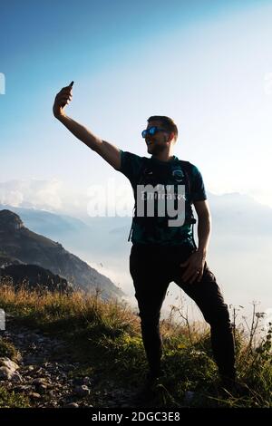 Sportivo attraente uomo spara selfie su montagna, giovane uomo con occhiali da sole Foto Stock