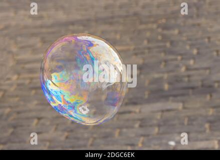 Bolla di sapone grande iridescente con un primo piano iridescente contro uno sfondo di piastrelle di pietra Foto Stock