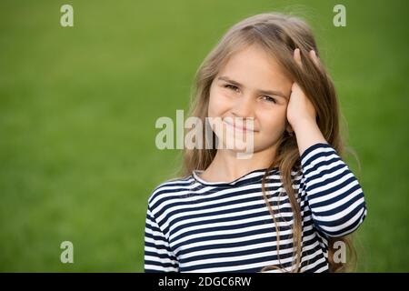 Sorriso felice piccolo capretto che corre le dita attraverso lunghi capelli biondi paesaggio naturale estivo, cura dei capelli, spazio di copia. Foto Stock