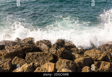 L'onda bianca del mare azzurro è rotta intorno al marrone della riva pietre grecia crit Foto Stock