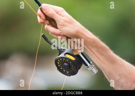 Uomo pesca a mosca con bobina e canna. Sport Fly fisher uomo primo piano su bobina. Foto Stock