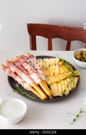 Pane grissini con pancetta, diversi tipi di formaggio e germogli di piselli, salsa e olive su fondo bianco di legno Foto Stock