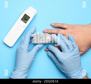 il processo di misurazione del livello di ossigeno nel sangue con un dito, accanto a un termometro elettronico senza contatto, primo piano Foto Stock