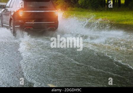 Irrorazione dell'acqua di un'auto in movimento su strada allagata durante l'alluvione causata da piogge torrenziali. Le auto galleggiano in acqua, allagando Foto Stock