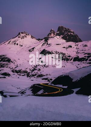 Auto sentieri luci su curve strada contro le montagne innevate durante l'alba al col du Pourtalet, Laruns, Francia Foto Stock