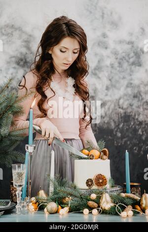 La ragazza taglia la torta di natale su un tavolo fisso Foto Stock