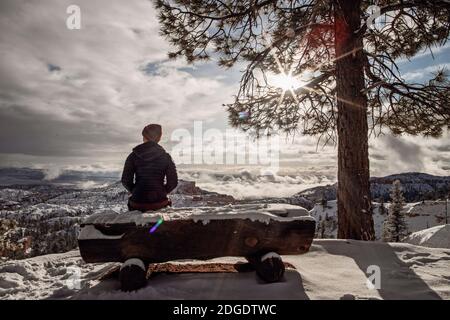 Donna si siede su panca coperta di neve che domina Bryce Canyon dopo neve Foto Stock