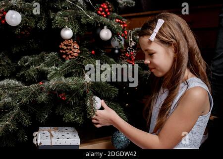 La bambina decora l'albero di Natale nel soggiorno di casa. Carino capretto che si prepara a casa per la celebrazione di Natale. Vacanze invernali e concetto di persone Foto Stock