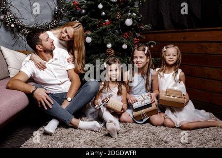 Felice famiglia carina con tre bambini che scambiano regali sotto l'albero di Natale sul tappeto. Concetto di famiglia e vacanza. Foto Stock