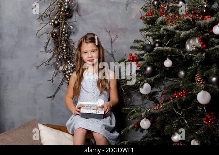 Carina ragazza che tiene scatole regalo di Natale e sorridente di fronte all'albero di Natale. Concetto di Natale o Capodanno. Foto Stock