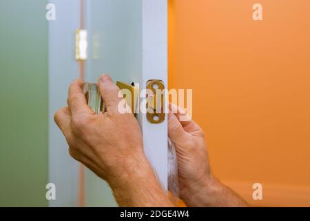 L'operatore ripara la serratura della portiera nelle mani del lavoratore installando una nuova armadietto della porta Foto Stock