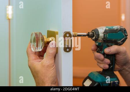 Uomo che ripara la chiocoseup della manopola della porta delle mani di lavoro che installa nuovo armadietto della porta Foto Stock