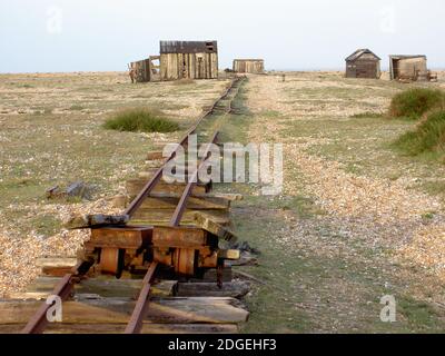 Una vecchia ferrovia dismessa, usata per portare i pescatori a recuperare la spiaggia di ciottoli a Dungeness, passa le capanne abbandonate sulla strada per il mare. Foto Stock