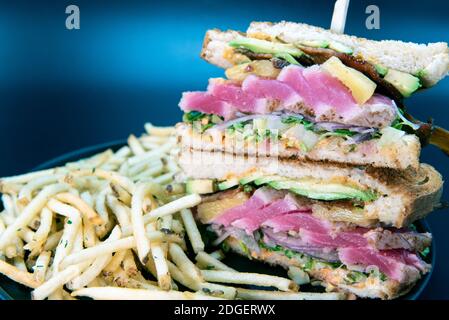 Alto ordine di panino Ahi Tuna Club e patatine fritte caricato con tutti i condimenti che l'impasto affollato brindano il pane può contenere Foto Stock