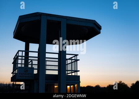 Una silhouette della torre di bagnino contro un cielo di tramonto colori giallo blu vividi con spazio di copia per l'annuncio di testo a Plovdiv, Bulgaria Foto Stock