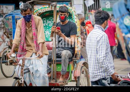 Una maschera che indossa il passeggero che viene tirato da una maschera che indossa un estrattore di risciò per le strade di Dhaka in Bangladesh. I risciò sono tricicli alimentati a pedale, ma usati per essere tirati a mano, da qui 'estrattore di risciò'. Oggi molti dei risciò sono persino convertiti per essere alimentati da un motore elettrico. Foto Stock