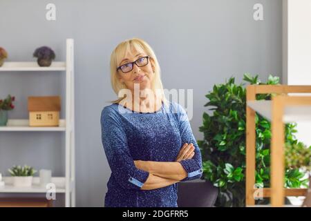 Ritratto di donna matura sorridente di mezza età con occhiali che guardano la macchina fotografica con le braccia incrociate. Foto Stock