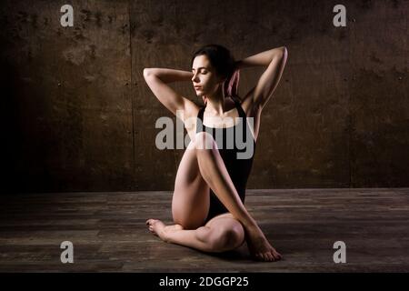 Bella giovane ballerina con lunghi capelli che scorrono in abiti neri, un costume da bagno ginnico, in una posa da ballo su un wit di legno pavimento Foto Stock