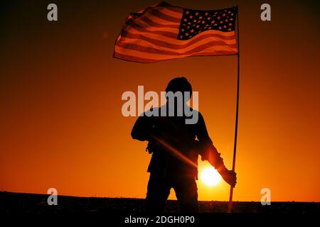 Silhouette del soldato dell'esercito degli Stati Uniti, sparatutto per operazioni speciali che tiene sventolare la bandiera nazionale flagpole mentre si trova sullo sfondo del tramonto. Eroe dell'esercito americano, vittoria militare degli Stati Uniti o dell'America Foto Stock