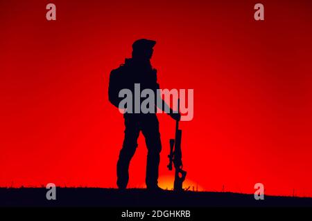 Silhouette di esercito speciale forze cecchino in piedi con fucile sullo sfondo del cielo tramonto. Combattente Commando in boonie cappello e area di pattugliamento munizioni di notte. Caccia Hunter al tramonto o all'alba Foto Stock