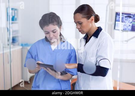 Personale sanitario in ufficio di stomatologia parlando di procedura di guarigione del capezzolo. Specialista ortodontico e assistente di clinica dentale che discute circa il trattamento dei denti. Foto Stock