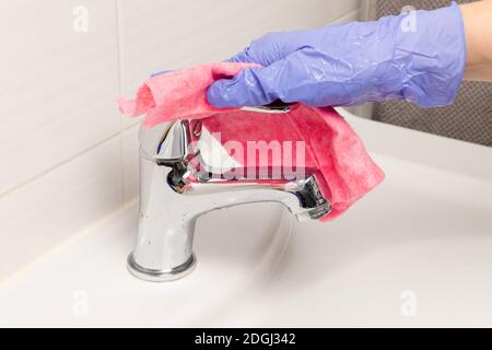 la mano femminile in un guanto blu strofina il mixer con uno straccio rosso in bagno. Pulizia della casa Foto Stock