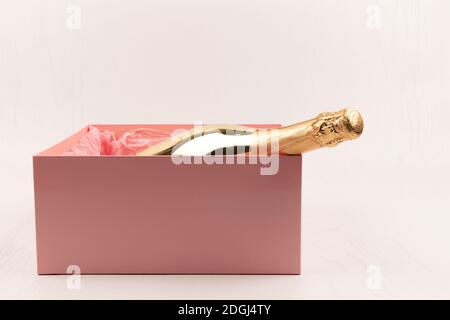 una bottiglia d'oro di champagne si trova in una scatola rosa regalo su uno sfondo bianco tavolo di legno Foto Stock