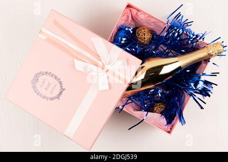 una bottiglia d'oro di champagne si trova in un regalo rosa Scatola con un arco e una tindel di Natale blu su un sfondo bianco della tabella Foto Stock