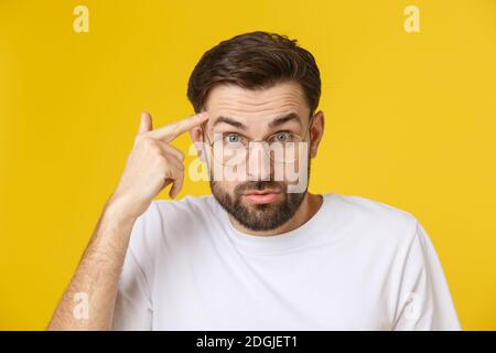 Primo piano di giovane bell'uomo che guarda e mostra il volto divertente alla macchina fotografica, indossando il vetro. Vista isolata su sfondo giallo. Foto Stock