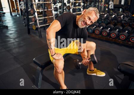 Bodybuilder sorridente dai capelli grigi che fa la ricciolo di concentrazione Foto Stock