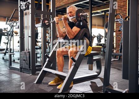 Allegro uomo dai capelli grigi che esegue l'esercizio bicipite Foto Stock