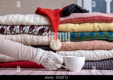 Un lotto di pullover e pullover diversi colori piegati in due pile e a mano con tazze di caffè. Foto Stock