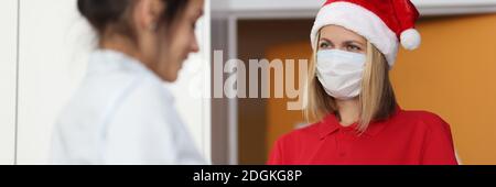 Courier donna in rosso babbo natale cappello e protettivo medico maschera su faccia dà al cliente di firmare documento e regalo Foto Stock