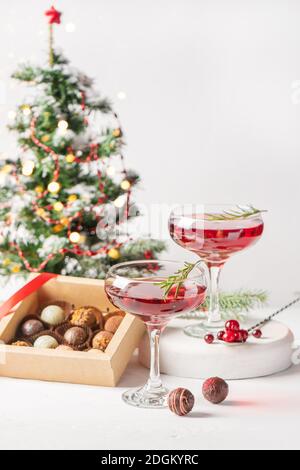 Cocktail invernale con rosmarino di mirtilli in due eleganti bicchieri su una scatola di cioccolatini di fondo bianco. Impostazione del tavolo di Natale o Capodanno. V Foto Stock