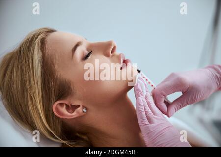 Cosmetologo professionista che inietta un riempitivo dermico nelle labbra del paziente Foto Stock