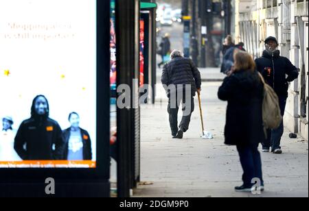 Londra, Inghilterra, Regno Unito. Uomo anziano con gambe a gomito e un bastone a piedi in Marylebone Road. Dic 2020 Foto Stock