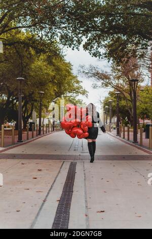 La splendida Brunette ispanica celebra il giorno di San Valentino con una dozzina Palloncini con cuore rosso Foto Stock