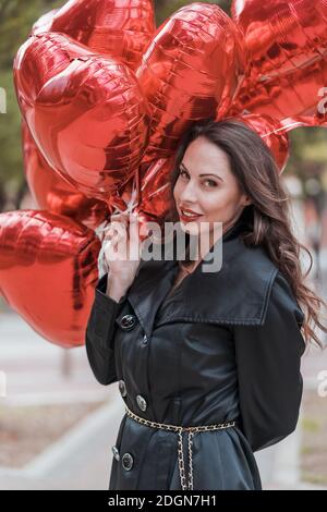 La splendida Brunette ispanica celebra il giorno di San Valentino con una dozzina Palloncini con cuore rosso Foto Stock