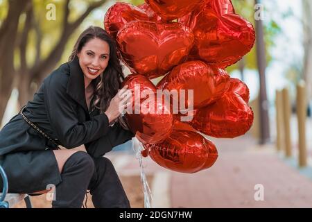 La splendida Brunette ispanica celebra il giorno di San Valentino con una dozzina Palloncini con cuore rosso Foto Stock