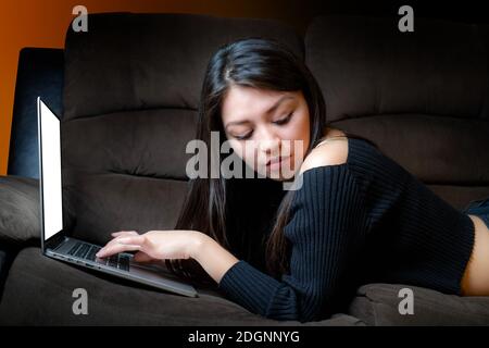 Giovane donna sorridente di fronte al computer su cui si riposa un divano Foto Stock