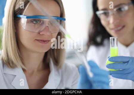 Scienziati femminili che versano il liquido chimico dalla pipetta nella provetta in laboratorio Foto Stock