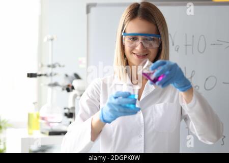 Donna scienziata in occhiali di sicurezza versando la soluzione chimica dal matraccio in laboratorio Foto Stock