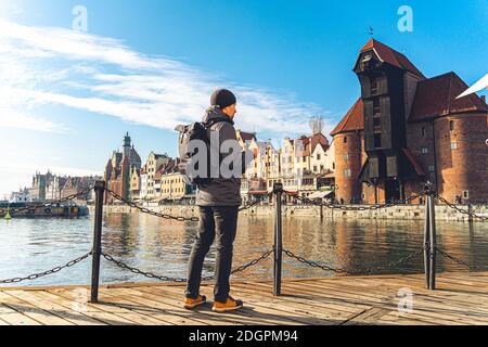 Tema del turismo in Polonia. Viaggiare a Danzica. Un viaggiatore maschile utilizza un telefono cellulare sull'argine del fiume Mottlawa in mezzo al ma Foto Stock