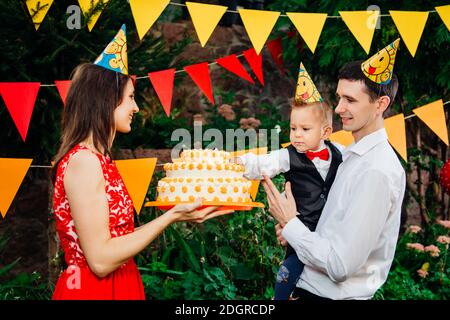 Soggetto festa di compleanno dei bambini, cibo e dolci. Una giovane famiglia celebra un anno di figlio. Papà sta tenendo una torta grande, mamma è Foto Stock