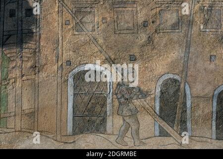 L'arte dello Sgraffito sull'antica casa borghese nel sito patrimonio dell'umanità dell'UNESCO di Telc, la regione di Vysocina, la Cechia o la Repubblica Ceca, raffigura la casa quando fu costruita per la prima volta, con merlature attiche e un costruttore o un ponteggio che camminano di fronte con un lungo palo in legno sulla spalla. Opere d'arte tra rari disegni sgraffiti della fine del XVI secolo scoperti sulle pareti nel 1952. Foto Stock