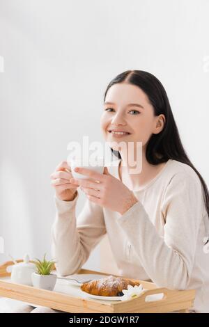 donna felice con vitiligine che tiene una tazza di tè vicino a colazione sul vassoio Foto Stock